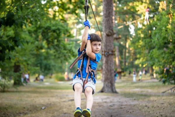 smiling boy rides a zip line. happy child on the zip line. The kid passes the rope obstacle course.