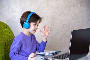 Evde dizüstü bilgisayarla oturup ders çalışırken kameraya bakan yakışıklı bir Avrupalı çocuk. Modern eğitim ve çalışma kavramı.