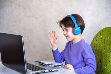 Evde dizüstü bilgisayarla oturup ders çalışırken kameraya bakan yakışıklı bir Avrupalı çocuk. Modern eğitim ve çalışma kavramı.