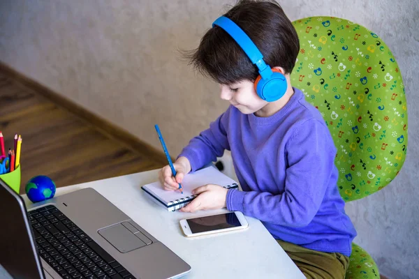 technology, home education and people concept - boy in headphones having classes trough internet on laptop computer at home. Lockdown remote safe communication.