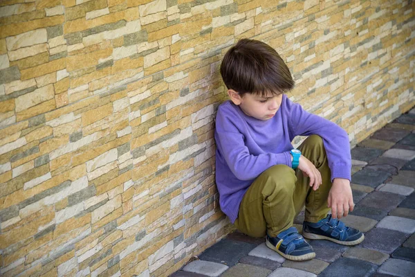 Little boy sad sitting alone at school hides his face. Isolation and bullying concept. Kid sad and unhappy, child was crying, upset, feel sick.