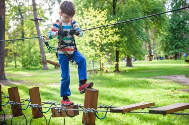Mutlu çocuk macera parkında oynuyor, ip tutuyor ve tahta merdivenlere tırmanıyor..