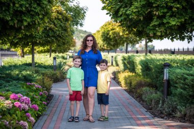 Genç bir kadın çocuklarıyla parkta oynarken eğleniyor. İlkokul çağındaki çocuklar. Aile pitoresk bitkilerle çevrili. Açık hava oyunları herkes için kullanışlı.