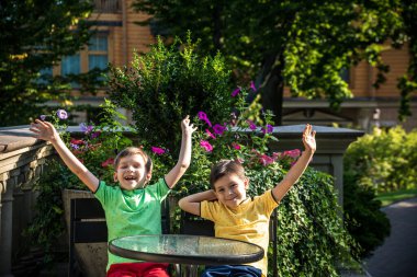İki küçük çocuk otel restoranında ya da şehir kafesinde sağlıklı bir kahvaltı için masada bekliyor. Çocuk rahat sandalyeye oturur, rahatlar, tatilinin tadını çıkarır. Çocuk konseptiyle yaz tatili.