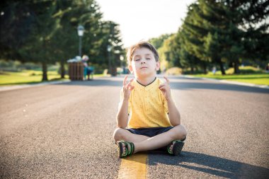 Bir çocuk yolun ortasında asfalt üzerinde oturmuş meditasyon yapıyor. Ruh eğitimi rahatlama kavramı.