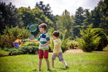 Heyecanlı bir çocuk baloncukların tadını çıkarırken çocuk sabun köpüğü üflüyor. Mutlu genç çocuk ve kardeşi parkta sabun köpüğü yapmayı seviyorlar. Mutlu çocukluk arkadaşlığı kavramı.