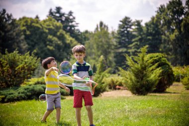 Heyecanlı bir çocuk baloncukların tadını çıkarırken çocuk sabun köpüğü üflüyor. Mutlu genç çocuk ve kardeşi parkta sabun köpüğü yapmayı seviyorlar. Mutlu çocukluk arkadaşlığı kavramı.