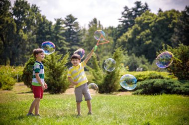 Heyecanlı bir çocuk baloncukların tadını çıkarırken çocuk sabun köpüğü üflüyor. Mutlu genç çocuk ve kardeşi parkta sabun köpüğü yapmayı seviyorlar. Mutlu çocukluk arkadaşlığı kavramı.