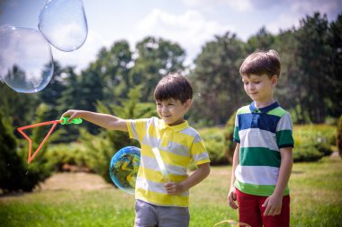 Heyecanlı bir çocuk baloncukların tadını çıkarırken çocuk sabun köpüğü üflüyor. Mutlu genç çocuk ve kardeşi parkta sabun köpüğü yapmayı seviyorlar. Mutlu çocukluk arkadaşlığı kavramı.