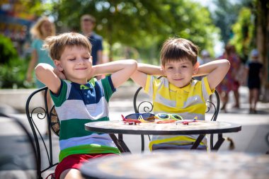 İki küçük çocuk otel restoranında ya da şehir kafesinde sağlıklı bir kahvaltı için masada bekliyor. Çocuk elleri havada rahat bir sandalyeye oturur, rahatlar ve tatilinin tadını çıkarır. Çocuk konseptiyle yaz tatili.