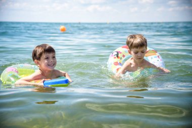 Mutlu çocuklar sahilde sörf yaparken eğleniyor. Şen şakrak bir çift çocuk kırılma dalgasında şişirilebilir ring gezintisinde. Seyahat yaşam tarzı, aile yaz kampında yüzme aktiviteleri. Tropikal adada tatiller.