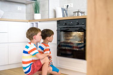 Çocuklar mutfakta oynuyorlar ve fırında bisküvi pişirmeyi bekliyorlar. İki kardeş evde yemek pişiriyor..