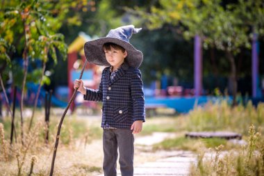 Sivri şapkalı çocuk dışarıda sihirli değnekle oynuyor. Küçük büyücü. Cadılar Bayramı konsepti.
