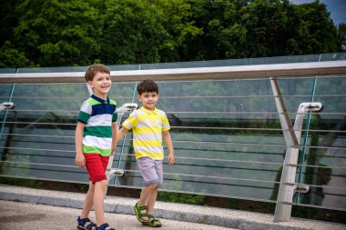 Köprüden aşağı bakan iki çocuğun portresi, güneşli bir günde dışarı çıkan çocuk, yazın cam köprüde dinlenen genç çocuklar. Turizm konsepti.