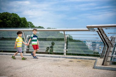 Köprüden aşağı bakan iki çocuğun portresi, güneşli bir günde dışarı çıkan çocuk, yazın cam köprüde dinlenen genç çocuklar. Turizm konsepti.