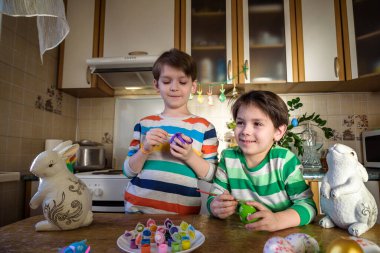 Paskalya tatili için ev mutfağında yumurta boyayan iki küçük çocuk. Kardeş kardeşler eğleniyor ve ziyafet çekiyorlar..