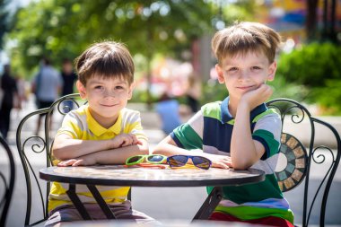İki küçük çocuk otel restoranında ya da şehir kafesinde sağlıklı bir kahvaltı için masada bekliyor. Çocuk rahat sandalyeye oturur, rahatlar, tatilinin tadını çıkarır. Çocuk konseptiyle yaz tatili.