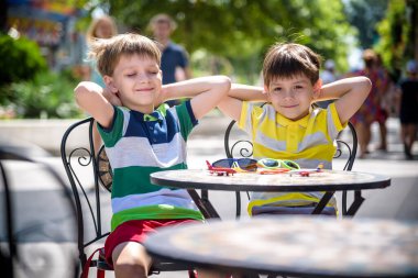 İki küçük çocuk otel restoranında ya da şehir kafesinde sağlıklı bir kahvaltı için masada bekliyor. Çocuk elleri havada rahat bir sandalyeye oturur, rahatlar ve tatilinin tadını çıkarır. Çocuk konseptiyle yaz tatili.