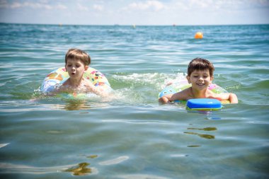 Mutlu çocuklar sahilde sörf yaparken eğleniyor. Şen şakrak bir çift çocuk kırılma dalgasında şişirilebilir ring gezintisinde. Seyahat yaşam tarzı, aile yaz kampında yüzme aktiviteleri. Tropikal adada tatiller.