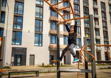 Şirin çocuk okul bahçesinde çocuk parkına tırmanıyor. Çok mutlu bir yüzü var ve bu macera sporlarını tek başına seviyor. Sıcak güneşli bir gün..