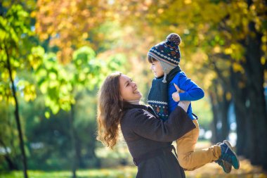 Sevimli, mutlu, gülümseyen ve sarı yaprakların arasında annesiyle kucaklaşan bir çocuk. Küçük çocuk annesiyle sonbahar parkında eğleniyor. Oğul ve ebeveyn arasındaki arkadaşlık kavramı, mutlu aile..