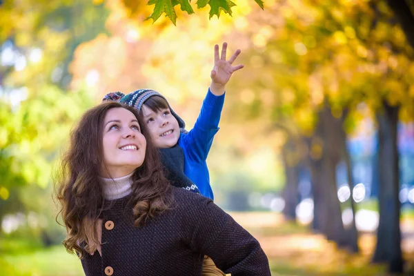 귀엽고 소년이 나뭇잎 사이에서 엄마와 껴안고 있습니다 공원에서 아이가 엄마와 — 스톡 사진