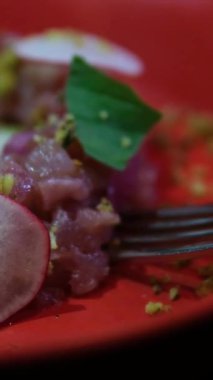 Delicate fish tartare made of raw minced fish beautifully plated on a red dish with radish greens and pistachios perfect for gourmet food photography culinary videos and restaurant menus.
