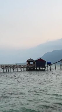 Phu Quoc Adası 'ndaki küçük bir balıkçı köyünde Vietnam tekneleri kıyıya yakın palmiye ağaçları ve günbatımı gökyüzü manzarası ve ahşap evleri olan yerel yaşam videoları..