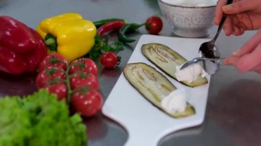 Vejetaryen kabağı ve peyniriyle patlıcan rulosu yapmak ve beyaz bir tabakta taze renkli sebzelerle doldurulmuş kavrulmuş kabak çekirdeği yapmak. Modern restoran mutfağı.