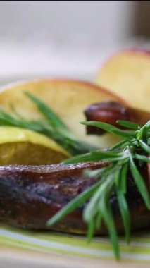 Elma ve biberiye ile ördek bacağı pişirme işlemi. Genç bir kadın yemek hazırlar, pişirir ve dekore eder. Ev yapımı kırsal mutfak atmosferini gösterir..