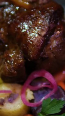 Bitmiş bir tabağın yakın çekimi. Kök sebzeli ve adaçaylı dana eti. Siyah tabakta patates ve salata ile dana bacağı, restoranda üç çeşit öğle yemeği.