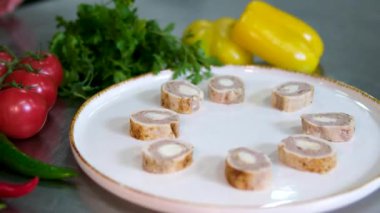 Beyaz bir tabağa yerleştirilmiş roka, sonra dilimlenmiş tavuk ve ciğer rulolarını domates dilimleriyle yerleştirilmiş olarak gösteren bir tarif. siyah ve beyaz susam ve zeytinyağı ile bitti..