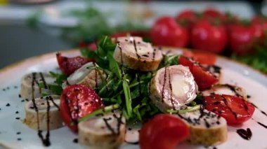 Beyaz bir tabağa yerleştirilmiş roka, sonra dilimlenmiş tavuk ve ciğer rulolarını domates dilimleriyle yerleştirilmiş olarak gösteren bir tarif. siyah ve beyaz susam ve zeytinyağı ile bitti..