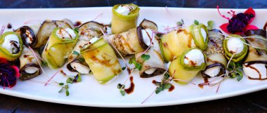 Vejetaryen kabağı ve peyniriyle patlıcan rulosu yapmak ve beyaz bir tabakta taze renkli sebzelerle doldurulmuş kavrulmuş kabak çekirdeği yapmak. Modern restoran mutfağı.