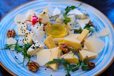 Krem peynirli, peynirli ve sert peynirli, böğürtlenli, fındıklı, yenilebilir çiçekler ve reçelli, mavi tabakta servis edilen çeşitli peynir tabağı. Peynirli fındıklı garnitür