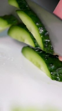 Ahşap mutfak tezgahında salatalık dilimleri ve koca bir tabak dolusu salatalıkla salatalığı ince parçalara ayırmak için bıçak kullanan kişinin yukarıdan görünüşü. Yüksek kalite 4k 