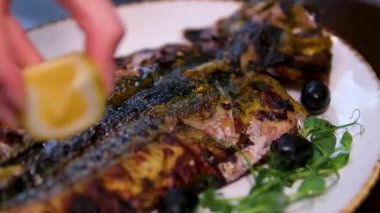 Siyah tabakta ızgara beyaz uskumru balığının üzerine limon suyu dökülmüş yakın çekim görüntüsü. Yüksek kalite 4k görüntü