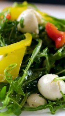 Arugula mozzarella salatası tabağında dilimlenmiş domatesli Caprese salatası, mozzarella topları ve taze bitkiler var. Parlak, güneşli bir gün. Yüksek kalite 4k görüntü
