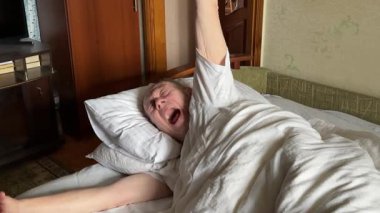 Üst düzey bir adam yatak odasında uyanıp esneyerek evde yenilenmiş bir sabah rutinini canlandırıyor. Yüksek kalite 4k görüntü