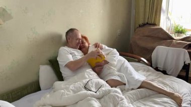 Yaşlı kadın kocasını dinlerken kitap okuyor, dükkandan alıyor ya da evine alıyor. Kütüphane, kanepede birlikte oturun, rahatlayın, kaygısız emeklilik hayatınızın ve favori hobinizin tadını çıkarın. Edebiyat, kitapçı reklamı.