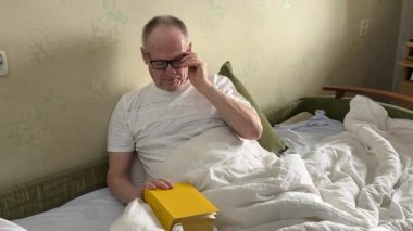 Geceleri kitap okumak. Gözlüklü siyahi bir adam boş vakitlerinde yatakta uzanıyor, yatak odasında ders çalışıyor. Yüksek kalite 4k görüntü