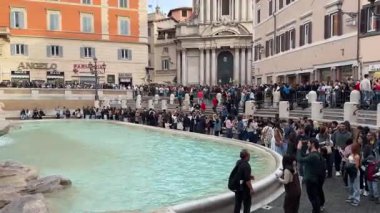 Roma 'daki Trevi Çeşmesi yakınlarında kalabalık içinde duran turistler, sembolik İtalyan anıtının fotoğraflarını çekmek için kuyrukta bekliyorlar. Bu durum, canlı atmosfer otantik seyahat deneyimini yansıtıyor. İtalya Roma' da 11.28.2025