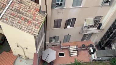 Yüksek bir terastan, sıcak bir teras çatısı olan bir İtalyan binasına bakıyor. Mimarisi detaylı ve ufka doğru yayılan küçük, dolambaçlı sokakları var..