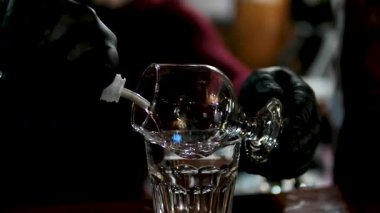 Kokteyl barı. Alkol içeceği hazırlanıyor. Barmen şişeden metal karıştırıcıya likör dolduruyor. Büyük buz küplü geniş kristal cam. Yüksek kalite 4k görüntü