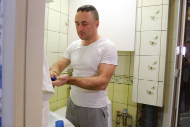 Beyaz adam, aynaya bakarak tıraş köpüğü ve fırçayla tıraş oluyor. Bir adam yüzünü duvarında kelebekler ve açık yeşil fayanslarla banyoda tıraş ediyor..