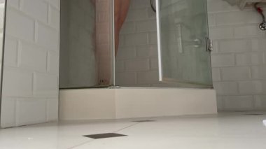 Kadının bacakları banyoya gider, havluyu indirir ve duşa girer. Yetişkin, kilolu bir kadının bacakları duştan çıkar.