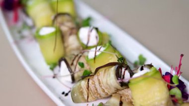 Aşçı şefi patlıcan kabaklı vejetaryen rulolarını kafede ceviz servis tabağıyla süslüyor, elleri siyah eldivenli yakın plan. Yemek servisi, restoranda yemek hazırlama. Sağlıklı organik ürünler.