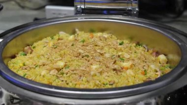 Büyük kızartma tavası. Bir tabak pirinç ve sebze. Buhar sıcak bir öğle yemeğinden geliyor. Ev mutfağı. Pilaf ahşap bir spatulayla karıştırılır. Misafirler çeşitli yemek büfelerinden hoşlanıyorlar. 