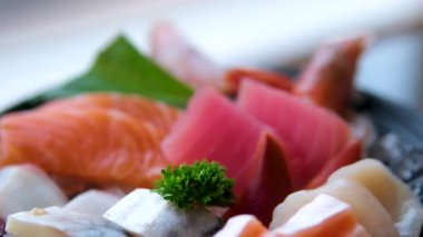 Canlı bir Japon saşimi tabağı somon, ton balığı, deniz tarağı ve somon yumurtası parlak, hatta ışık altında siyah bir zemin üzerinde yavaşça döner. Yüksek kalite 4k 
