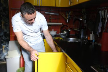 Dijital tablet üzerinde iletişim kuran neşeli adam sarı mutfakta yemek pişiriyor. Mutfakta tablet kullanan orta yaşlı bir adam internetten yemek pişirme süreci hakkında konuşuyor..